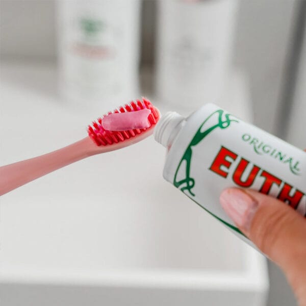 Brosse à dents Euthymol Whitening - Brosse à dents manuelle blanche avec technologie Flex-Firm pour une élimination en douceur de la plaque dentaire. Illustration brosse à dents avec dentifrice rose dessus